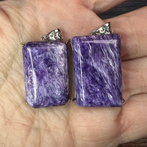 May include: Two purple and white gemstone pendants with silver settings. The pendants are rectangular and have a swirling pattern.
