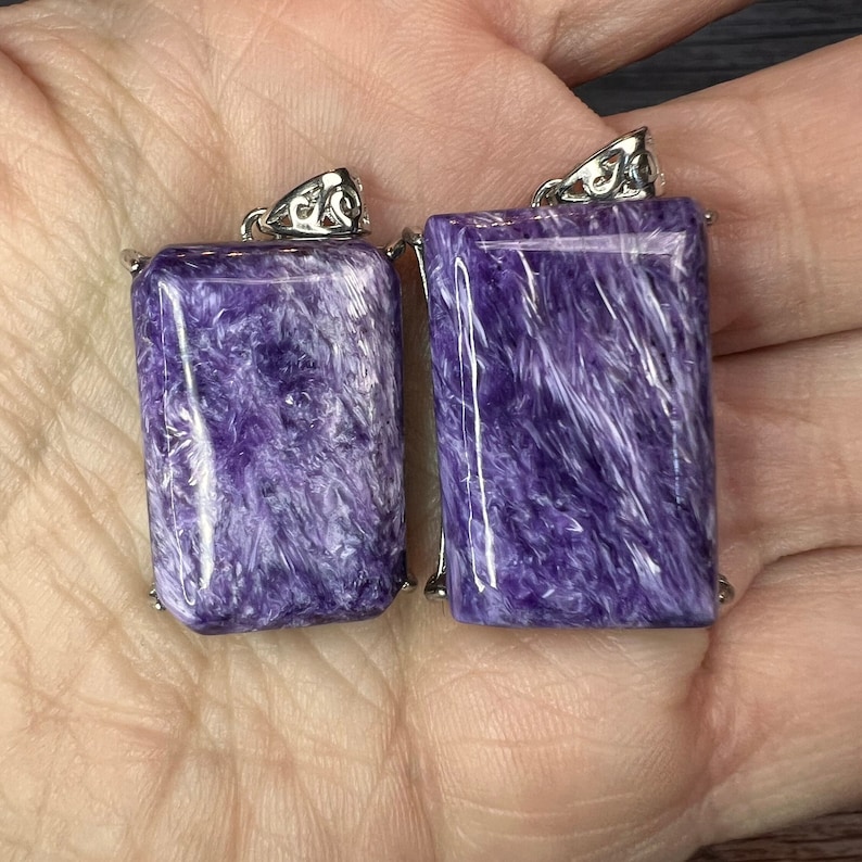 May include: Two purple and white gemstone pendants with silver settings. The pendants are rectangular and have a swirling pattern.