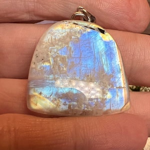 May include: A iridescent white gemstone pendant with a silver bail. The gemstone has a blue and yellow sheen.