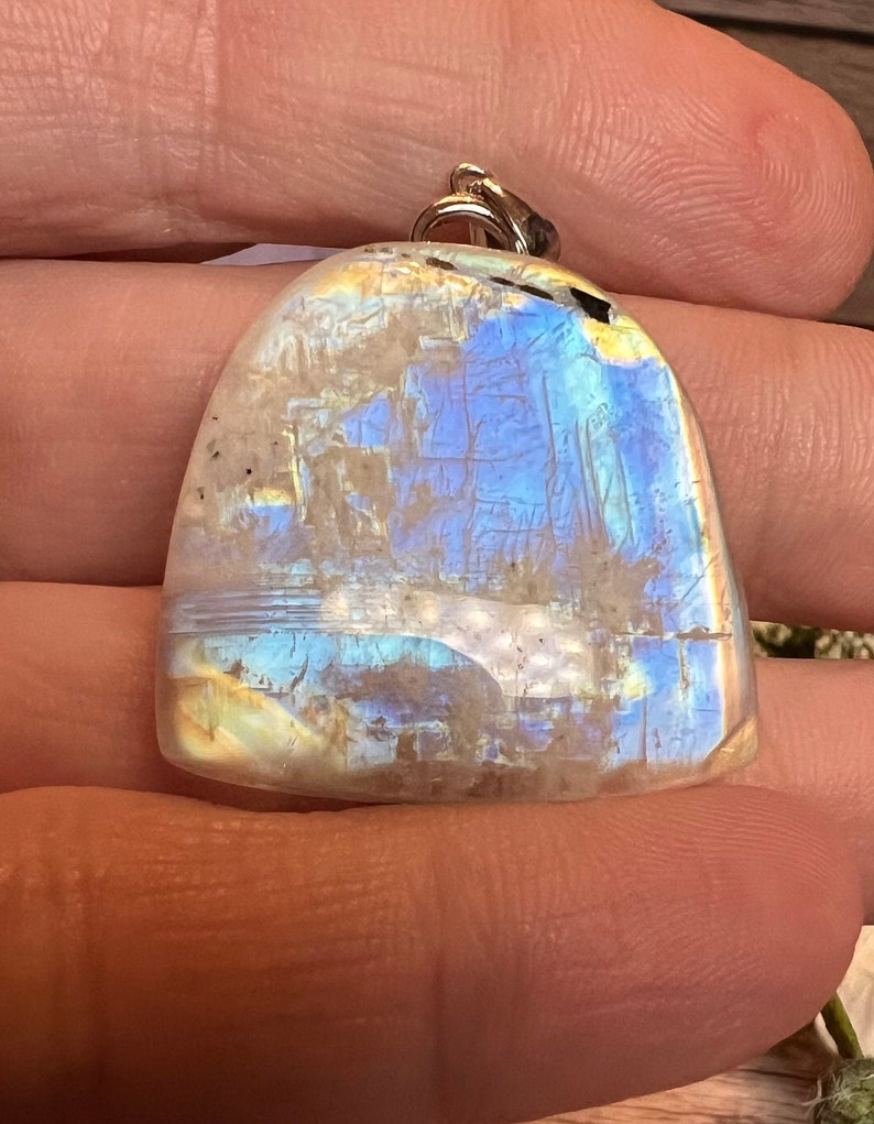 May include: A iridescent white gemstone pendant with a silver bail. The gemstone has a blue and yellow sheen.