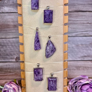 May include: Six purple and silver pendants on a wooden display stand. The pendants are made of a natural stone with a swirling pattern.
