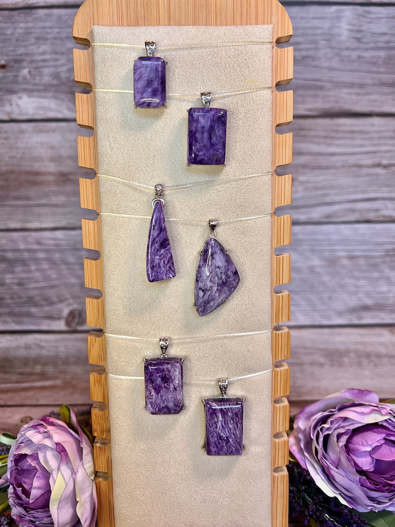 May include: Six purple and silver pendants on a wooden display stand. The pendants are made of a natural stone with a swirling pattern.