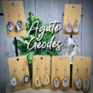 May include: Agate Geodes earrings.  The earrings are made of silver and feature a variety of agate geodes in different colors and patterns.  The earrings are displayed on a brown background.