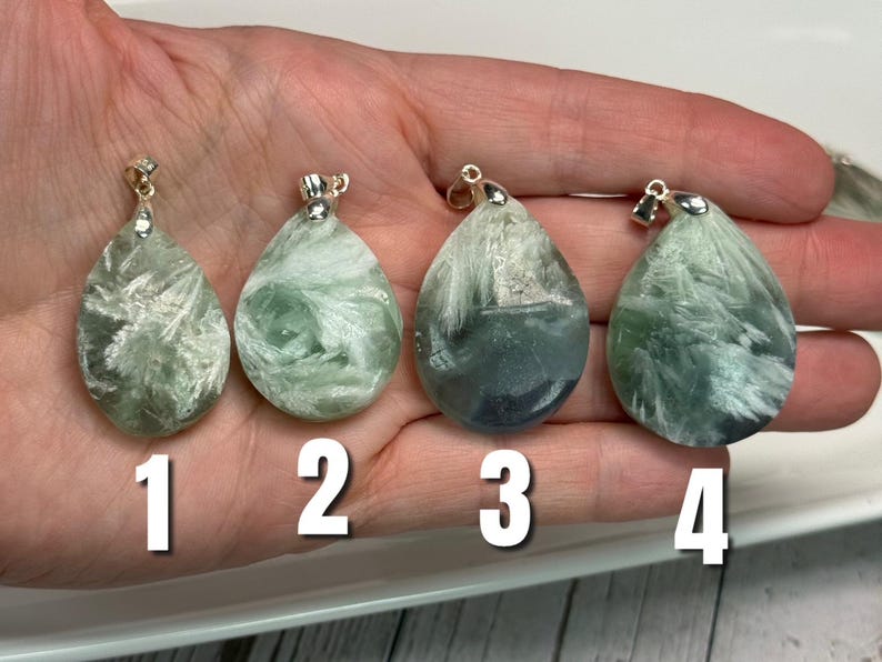 May include: Four teardrop-shaped pendants with silver-coloured bails. The pendants are a mix of green and white, with a feathery, textured appearance. Each pendant is numbered 1 through 4 in white. The pendants are displayed on a hand.