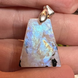 May include: A silver pendant with a large, iridescent, triangular moonstone. The stone has a white base with blue, green, and gold iridescence.