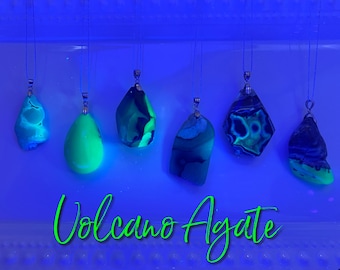 May include: Six green and blue volcano agate pendants with silver bail, hanging from strings against a blue background. The text "Volcano Agate" is written in green cursive below the pendants.