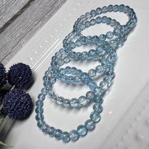 May include: Four light blue aquamarine gemstone bracelets stacked on a white plate. The bracelets are made of round beads.