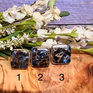 May include: Three square-shaped rings with a mosaic of blue, brown, and gold stones. The rings are numbered 1, 2, and 3.