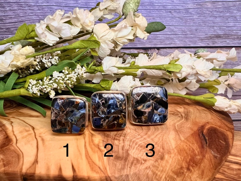 May include: Three square-shaped rings with a mosaic of blue, brown, and gold stones. The rings are numbered 1, 2, and 3.
