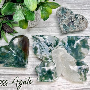 May include: Three moss agate heart-shaped dishes, one in the shape of a butterfly, with green and white patterns. Moss agate is a type of chalcedony with green inclusions that resemble moss.
