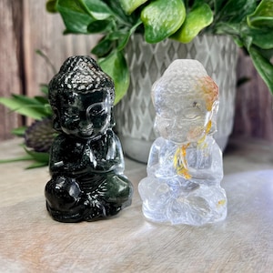 May include: Two small meditating Buddha statues, one carved from black stone and the other from clear quartz with yellow inclusions.