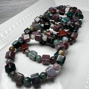 May include: A set of four bracelets made with square-shaped, multi-colored agate beads. The beads are a mix of green, brown, red, and purple.