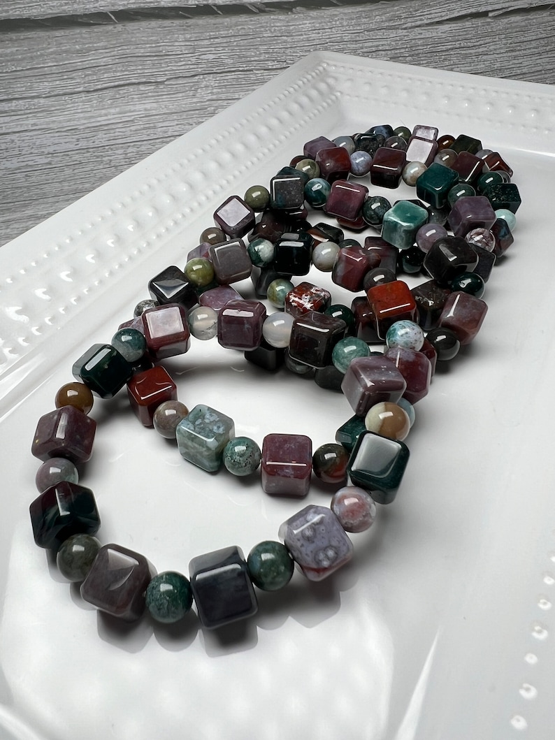 May include: A set of four bracelets made with square-shaped, multi-colored agate beads. The beads are a mix of green, brown, red, and purple.