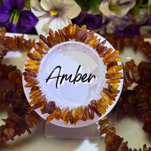May include: A collection of amber bracelets. Each bracelet is made of irregular, polished amber pieces in shades of brown and yellow. The word "Amber" is written in cursive on a white background.