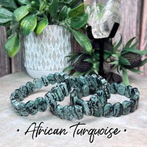 May include: Three green and black African turquoise bracelets stacked on a wooden surface. The bracelets are made of oval-shaped beads.