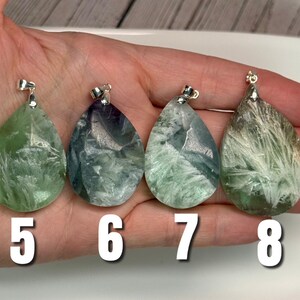 May include: Four teardrop-shaped fluorite pendants with silver bails. The pendants display green, blue, and purple hues with crystalline patterns. Numbers 5, 6, 7, and 8 are printed in white below the pendants.