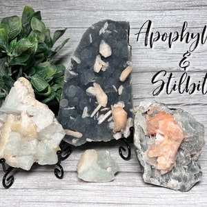 May include: A collection of Apophyllite and Stilbite crystals. The crystals are a variety of colors, including green, white, and orange. The crystals are displayed on small black metal stands.
