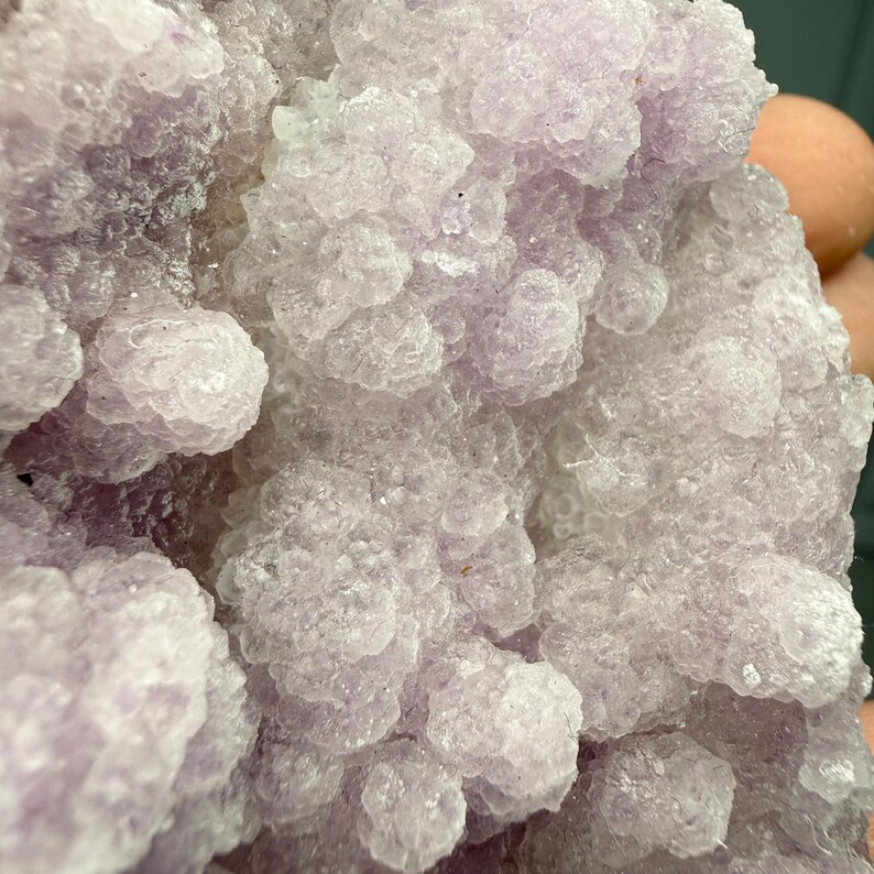 May include: Close-up of a cluster of light purple crystals. The crystals have a bubbly, rounded texture, with a slightly translucent appearance. The overall color is a soft, pale lavender, with variations in tone.