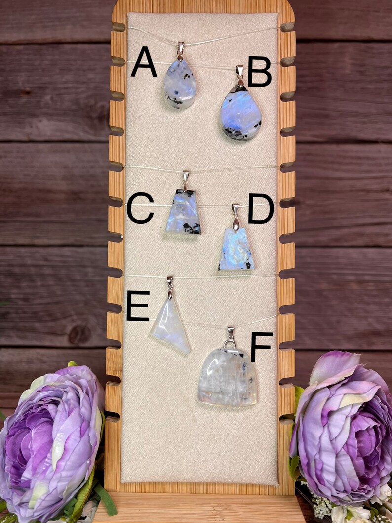 May include: Six rainbow moonstone pendants on display on a wooden stand. The pendants are labeled A through F.