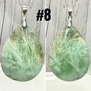 May include: A green, teardrop-shaped pendant with a silver bail. The stone has white, feathery patterns and a tan top. The image includes the number "#8" in black. The pendant is likely a piece of jewellery.