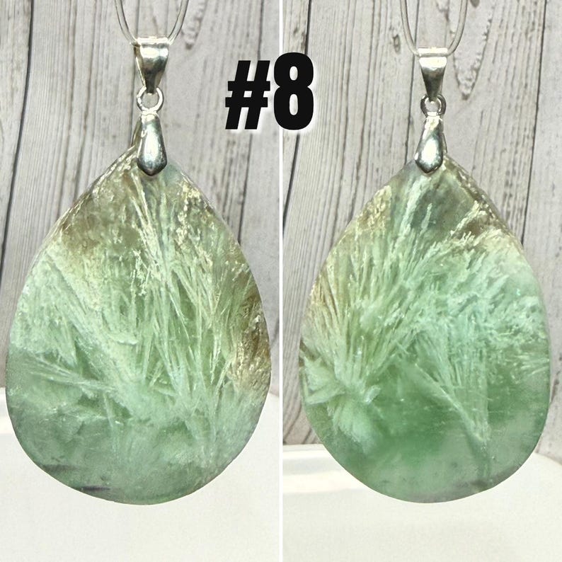 May include: A green, teardrop-shaped pendant with a silver bail. The stone has white, feathery patterns and a tan top. The image includes the number "#8" in black. The pendant is likely a piece of jewellery.