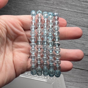 May include: Five strands of light blue aquamarine bead bracelets. The beads are round and have a translucent appearance.