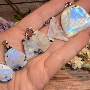May include: Five iridescent rainbow moonstone pendants with silver bail settings. The pendants are in various shapes, including teardrop, triangle, and freeform. The moonstone has a milky white color with flashes of blue and green.