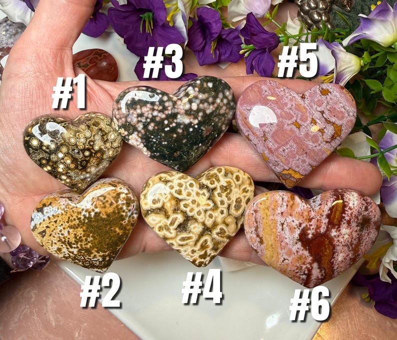 May include: Six heart-shaped stones in various colors and patterns. The stones include speckled, spotted, and marbled designs in shades of brown, green, pink, and white. Each stone is numbered from one to six.