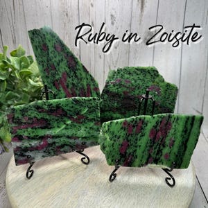 May include: Four pieces of ruby in zoisite gemstone displayed on black metal stands. The stones have a vibrant green base color with dark red and black inclusions. The text "Ruby in Zoisite" is written in cursive.