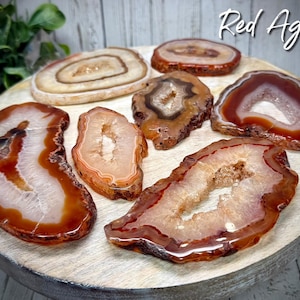 May include: A collection of six red agate slices with natural patterns and varying sizes. The slices are arranged on a wooden surface. Red Agate.