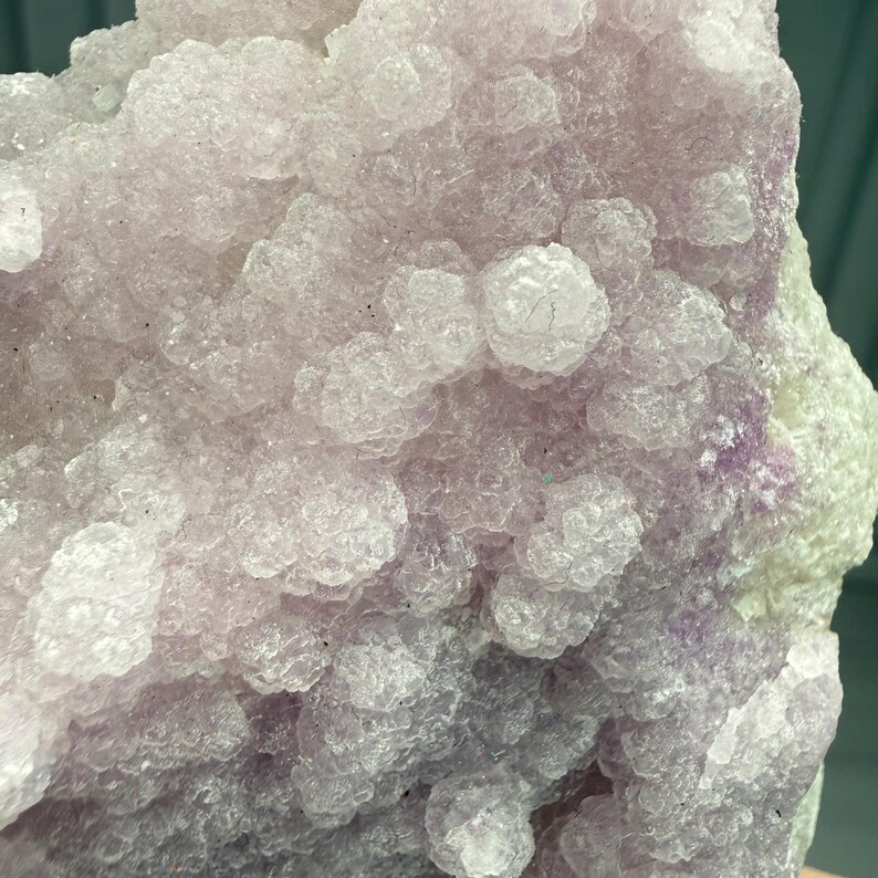 May include: Close-up of a cluster of light purple crystals with a bubbly, textured surface. The crystal formation has a soft, almost translucent appearance, with hints of darker purple and white.