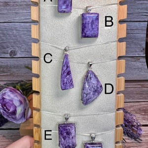 May include: Six purple and silver pendants on a wooden display stand. The pendants are labeled A through F.