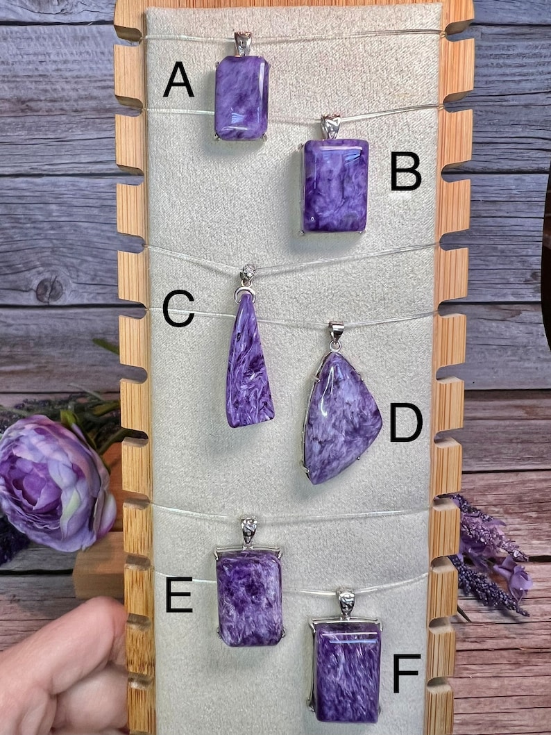 May include: Six purple and silver pendants on a wooden display stand. The pendants are labeled A through F.