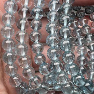 May include: A strand of light blue aquamarine beads, each bead is round and smooth. The beads are strung together on a clear thread.