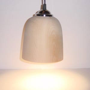 Könnte beinhalten: Eine Holz-Pendelleuchte mit einem verchromten Oberteil. Die Leuchte ist eingeschaltet und strahlt ein warmes Licht aus.