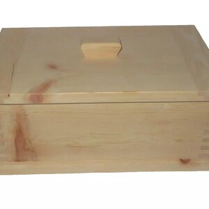 Könnte beinhalten: Eine natürliche Holzkiste mit einem Scharnierdeckel und einem einfachen rechteckigen Knopf. Die Kiste ist aus hellem Holz mit einer glatten Oberfläche.