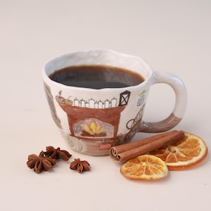 Pode incluir: Uma caneca de cerâmica cheia de líquido escuro, com um design de lareira pintado à mão com abóboras e velas. Acompanham a caneca anis estrelado, paus de canela e rodelas de laranja desidratada, criando um tema outonal.