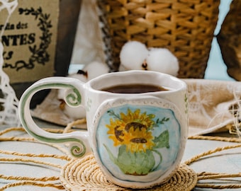 May include: A white ceramic mug with a sunflower design and a green handle. The mug is filled with dark brown coffee and is sitting on a woven straw coaster.