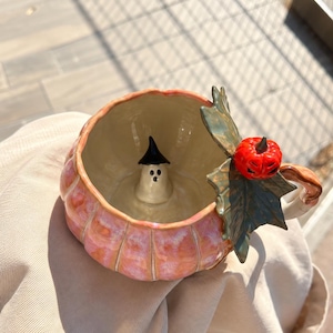 Peut inclure: Une tasse en céramique en forme de citrouille avec une finition rose et orange brillante. À l'intérieur, une petite figurine de fantôme blanc avec un chapeau noir est fixée au fond. Une feuille verte et une petite citrouille rouge ornent l'anse.