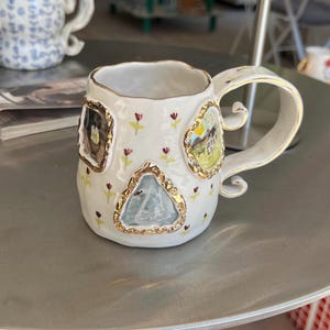May include: A set of three ceramic mugs with a speckled, matte finish. The mugs are in shades of cream, light gray, and dark gray. Each mug has a simple, minimalist design and a rounded handle.