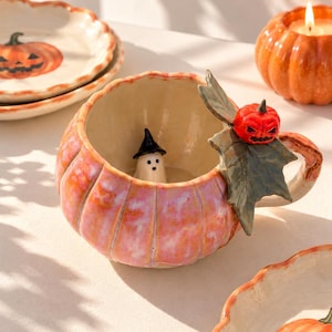 Peut inclure: Un mug en céramique en forme de citrouille avec une finition brillante rose et orange. L'anse présente une feuille verte sculptée et une petite citrouille rouge. À l'intérieur, une figurine de fantôme blanc avec un chapeau noir est posée.