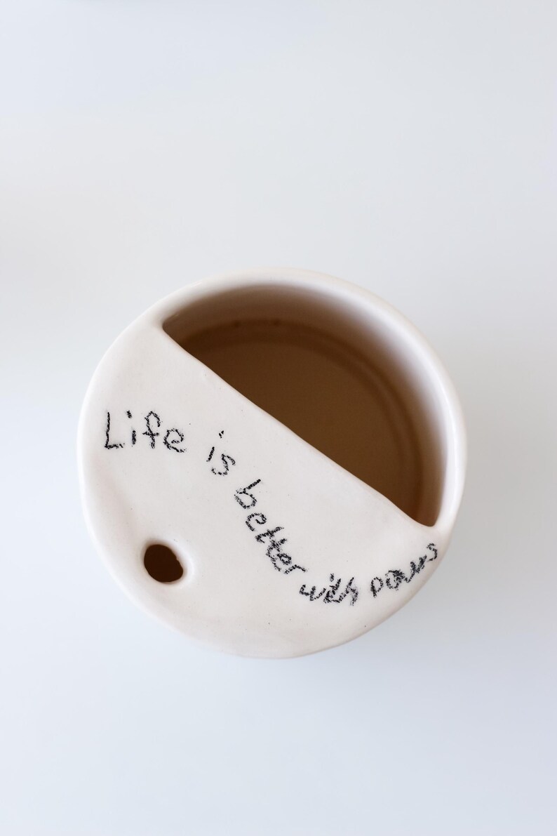 May include: White ceramic mug with a divided section and a hole in the bottom. The mug has the handwritten message "Life is better with paws" on the side.