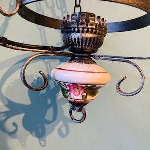 Puede incluir: Una lámpara de araña de estilo vintage con una pantalla de porcelana blanca con un diseño floral. La lámpara de araña está hecha de metal con un acabado gris oscuro y tiene una cadena que cuelga del techo.