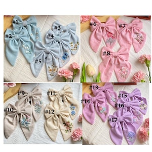 K&ouml;nnte beinhalten: Ein Set mit 17 handgefertigten Stoffhaarb&auml;ndern mit Blumenstickerei. Die Schleifen sind in Blaut&ouml;nen, Rosa und Beige gehalten. Jede Schleife ist von 1 bis 17 nummeriert.