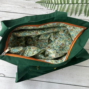 May include: A dark green tote bag with a zipper closure. The bag is lined with a floral fabric in shades of blue, green, and brown.