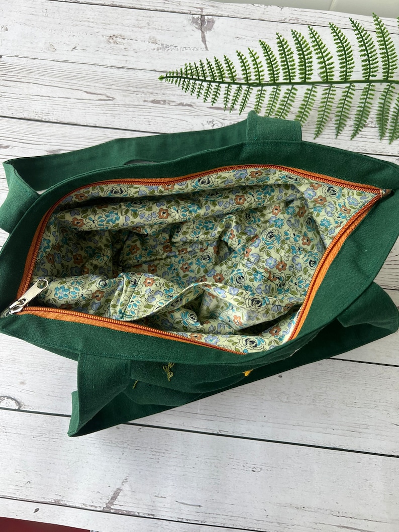 May include: A dark green tote bag with a zipper closure. The bag is lined with a floral fabric in shades of blue, green, and brown.