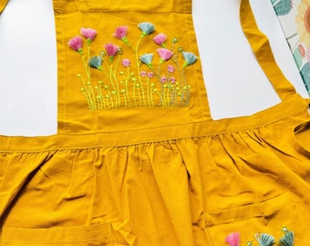 May include: A yellow apron with a floral embroidery design. The apron has two pockets and adjustable straps.