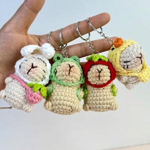 May include: Four handmade crochet keychains featuring animal designs. The keychains include a bunny, frog, strawberry, and chick, each with a unique outfit. The keychains are attached to silver metal key rings.