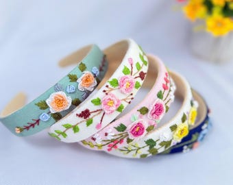 May include: A collection of floral embroidered headbands in various colors. The headbands feature detailed embroidery of pink, orange, and yellow flowers with green leaves. The headbands are in shades of blue, white, and pink.