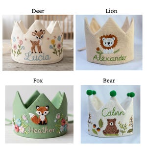 May include: Four embroidered fabric crowns with animal designs: a deer, a lion, a fox, and a bear. Each crown has a different color scheme and is personalized with a name. The deer crown is white with blue and pink flowers and the name "Lucia".